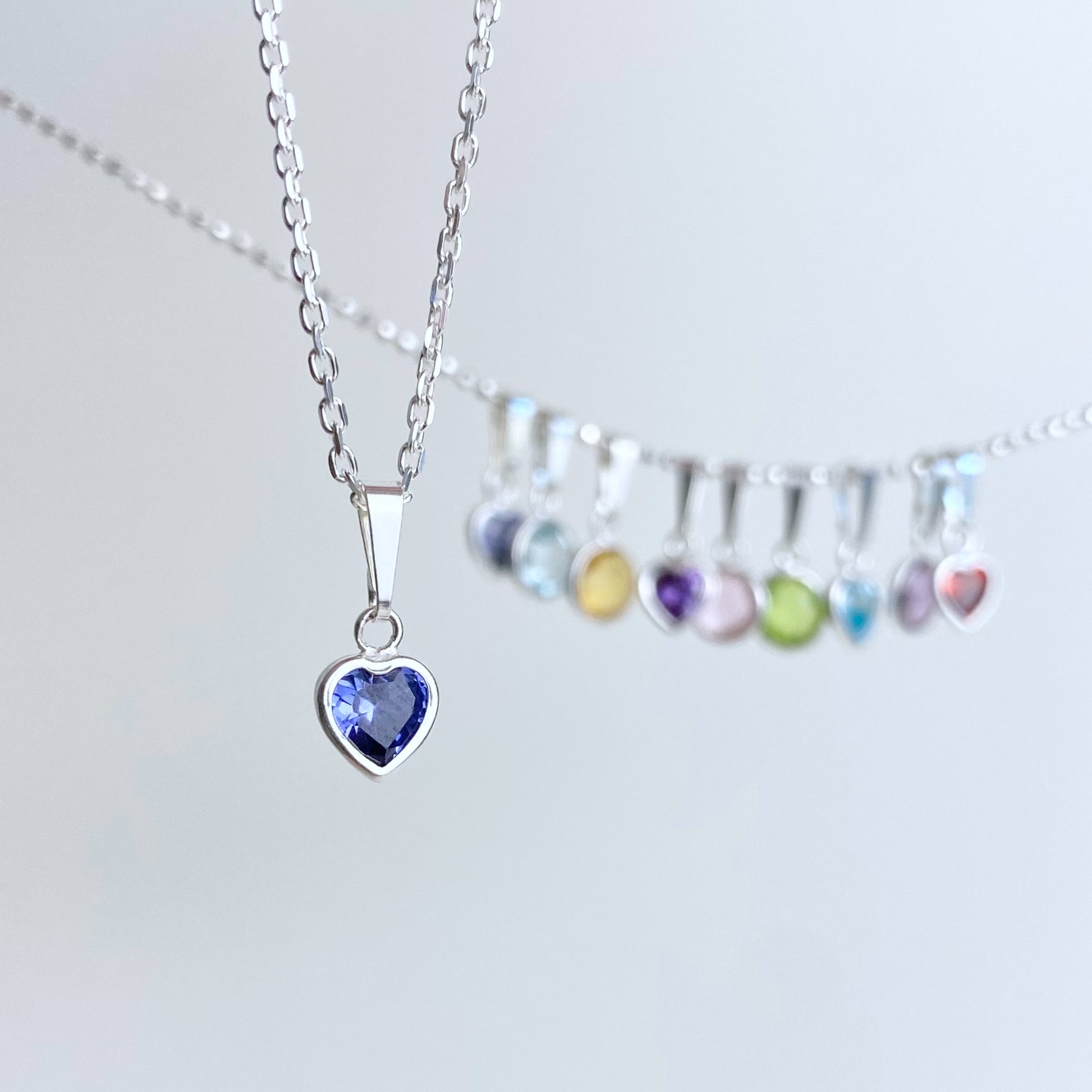 blauer herz Anhänger in 925 Silber vor unscharfen Charms mit bunten steinen