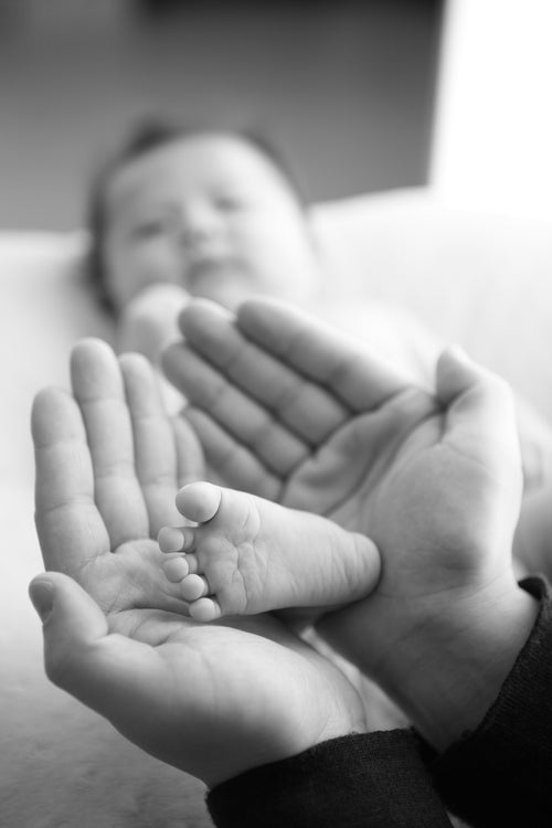 baby im hintergrund mit zwei händen welche babyfuß halten 